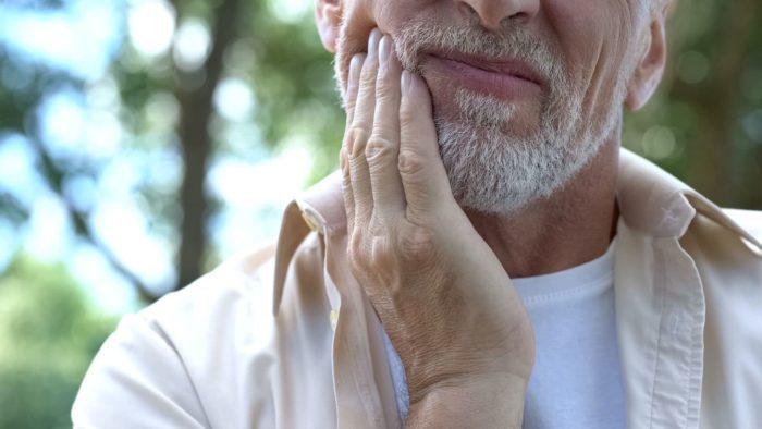 older man holding face in pain in need of root canal dentist Chevy Chase Maryland